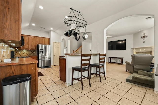 kitchen featuring light colored carpet, vaulted ceiling, an inviting chandelier, stainless steel fridge with ice dispenser, and a breakfast bar area