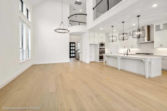 kitchen with decorative light fixtures, a towering ceiling, ventilation hood, and an island with sink