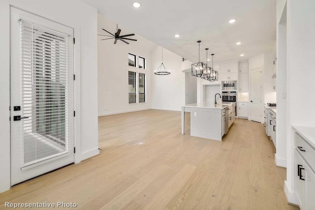 kitchen featuring a center island with sink, hanging light fixtures, light hardwood / wood-style floors, white cabinetry, and stainless steel appliances