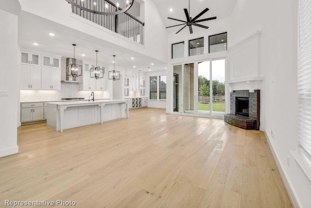 unfurnished living room with ceiling fan, sink, light hardwood / wood-style flooring, a fireplace, and a high ceiling