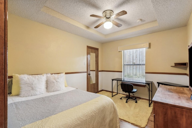 bedroom featuring a raised ceiling, ceiling fan, light hardwood / wood-style flooring, and a textured ceiling