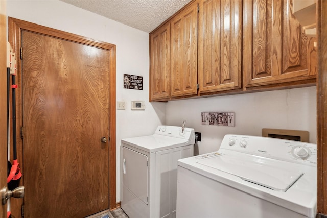 clothes washing area with washer and dryer, a textured ceiling, and cabinets