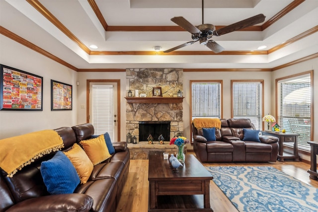 living room featuring ornamental molding, a tray ceiling, ceiling fan, hardwood / wood-style floors, and a stone fireplace