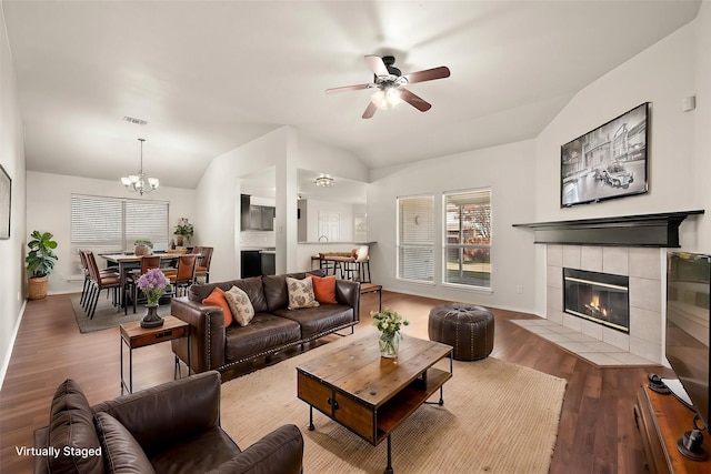 living room featuring ceiling fan with notable chandelier, hardwood / wood-style flooring, lofted ceiling, and a tiled fireplace