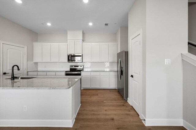 kitchen with light stone countertops, sink, appliances with stainless steel finishes, white cabinets, and hardwood / wood-style flooring