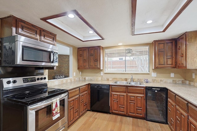 kitchen featuring a raised ceiling, sink, appliances with stainless steel finishes, and light hardwood / wood-style flooring