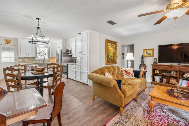 living room featuring ceiling fan with notable chandelier, wood-type flooring, and sink