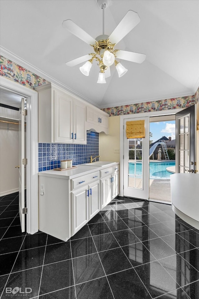 kitchen featuring lofted ceiling, sink, white cabinetry, crown molding, and backsplash