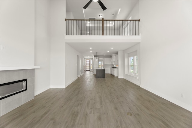 1514 Overton St, Frisco, TX 75036 - unfurnished living room featuring a ceiling fan, a high ceiling, a tile fireplace, wood finished floors, and baseboards
