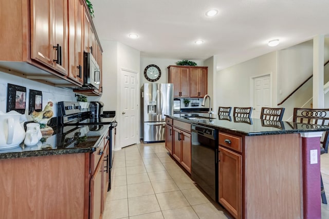 kitchen featuring sink, appliances with stainless steel finishes, a kitchen island with sink, dark stone countertops, and a kitchen bar