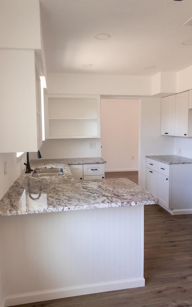 kitchen with white cabinets, sink, light stone counters, dark hardwood / wood-style flooring, and kitchen peninsula