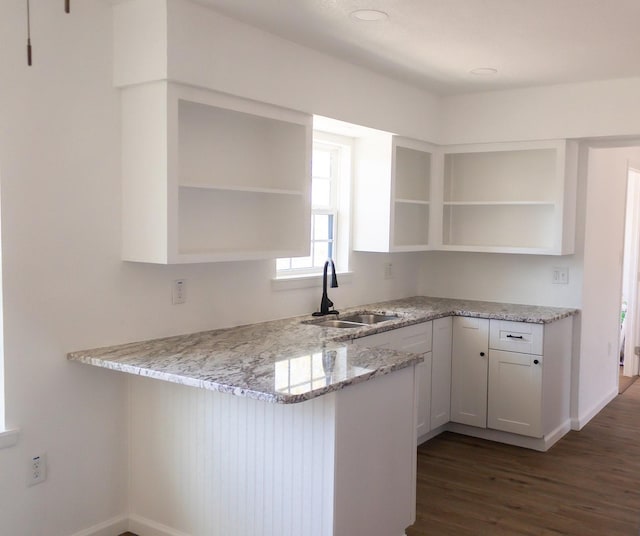 kitchen with white cabinetry, sink, light stone counters, dark hardwood / wood-style floors, and kitchen peninsula