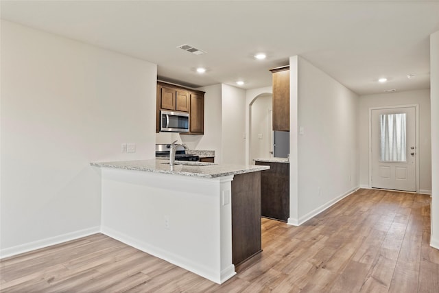 kitchen with kitchen peninsula, appliances with stainless steel finishes, light hardwood / wood-style floors, and light stone countertops