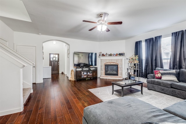 living area featuring arched walkways, wood-type flooring, a fireplace, and a ceiling fan