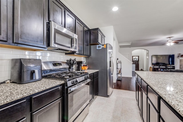 kitchen featuring appliances with stainless steel finishes, tasteful backsplash, light hardwood / wood-style floors, light stone counters, and dark brown cabinetry