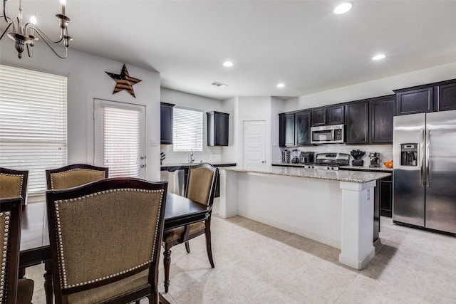 kitchen with pendant lighting, a center island, light stone countertops, tasteful backsplash, and stainless steel appliances