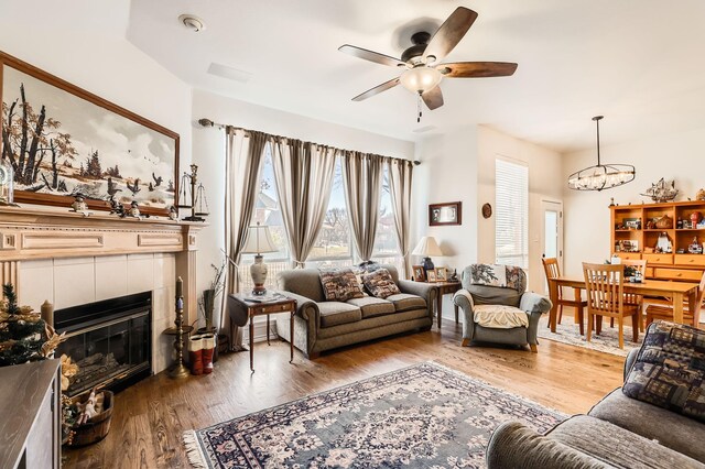 living room featuring a tile fireplace, hardwood / wood-style floors, and ceiling fan with notable chandelier