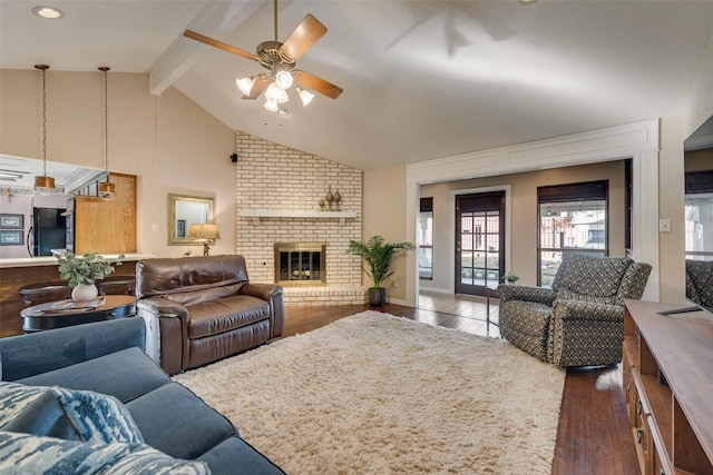 living room with a brick fireplace, ceiling fan, dark wood-type flooring, beam ceiling, and high vaulted ceiling