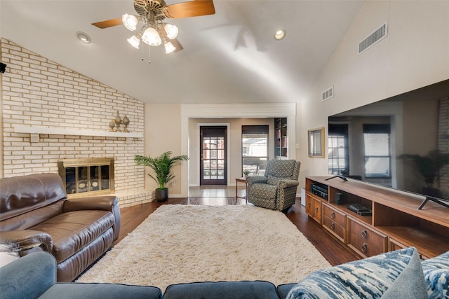 living room with ceiling fan, dark hardwood / wood-style flooring, high vaulted ceiling, and a brick fireplace