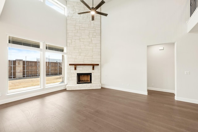 unfurnished living room with a high ceiling, dark wood-style flooring, a fireplace, and a healthy amount of sunlight