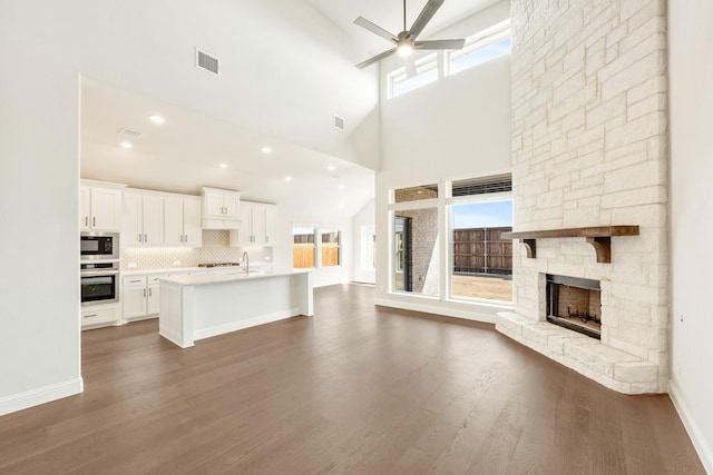 unfurnished living room with visible vents, baseboards, dark wood-style floors, ceiling fan, and a fireplace