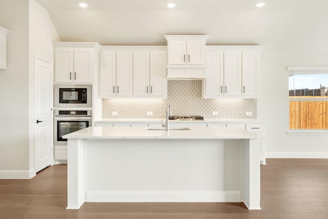 kitchen featuring a center island with sink, light countertops, a sink, black microwave, and oven