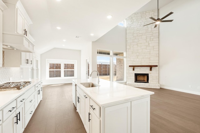 kitchen with wood finished floors, a sink, open floor plan, decorative backsplash, and stainless steel gas stovetop