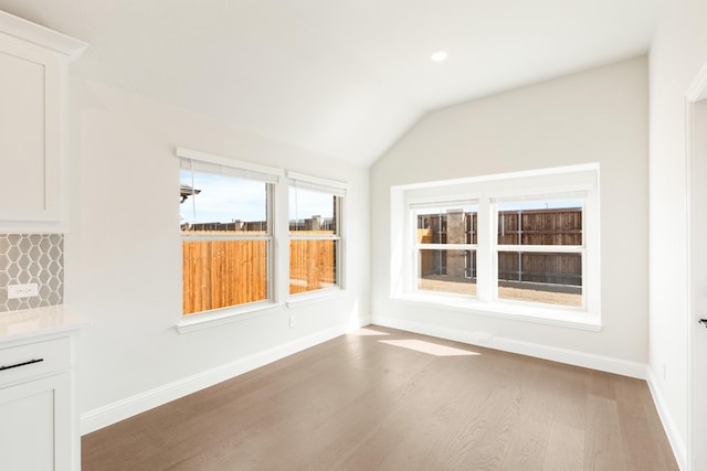 spare room featuring vaulted ceiling, wood finished floors, and baseboards