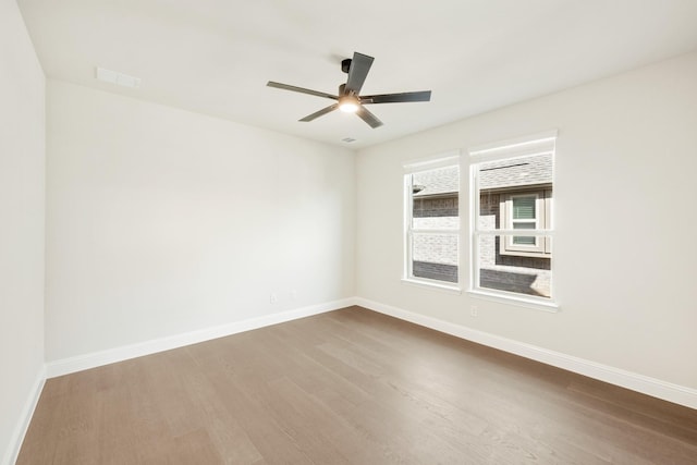 empty room with ceiling fan, wood finished floors, visible vents, and baseboards