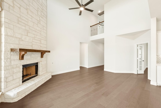 unfurnished living room with ceiling fan, visible vents, wood finished floors, and a stone fireplace