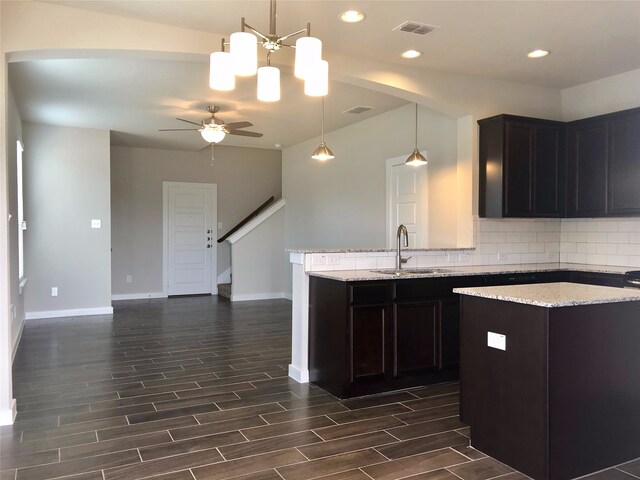 kitchen featuring light stone countertops, sink, dark wood-type flooring, pendant lighting, and decorative backsplash