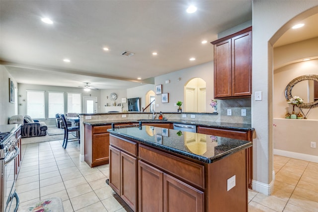 kitchen with ceiling fan, light tile patterned floors, backsplash, dark stone countertops, and a kitchen island