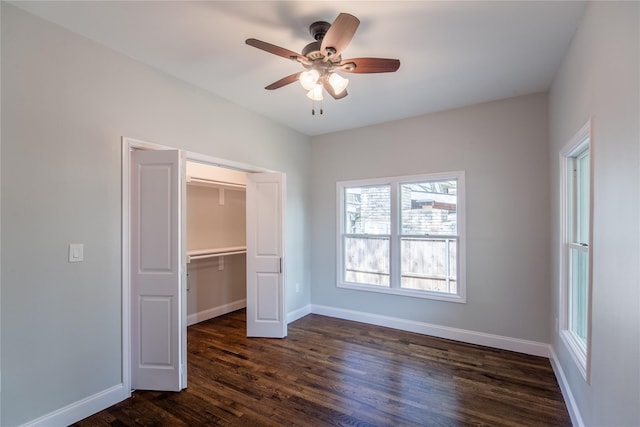 unfurnished bedroom with a walk in closet, a closet, ceiling fan, and dark wood-type flooring