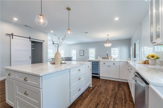 kitchen with white cabinets, hanging light fixtures, stainless steel dishwasher, a barn door, and dark hardwood / wood-style flooring