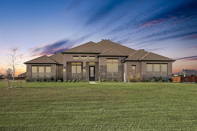 view of front of house with a shingled roof, brick siding, fence, and a lawn