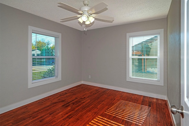 unfurnished room with a wealth of natural light, ceiling fan, dark wood-type flooring, and a textured ceiling