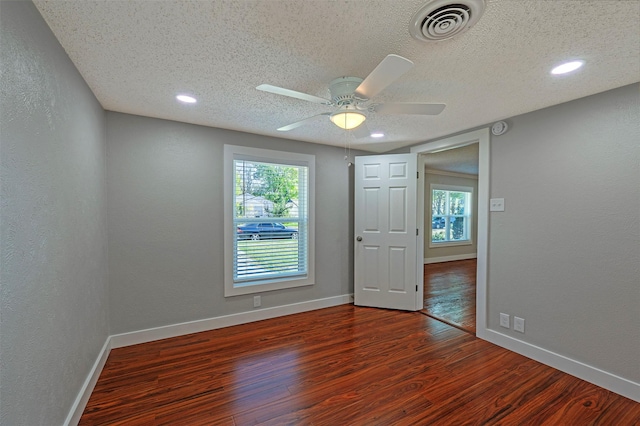 spare room featuring a healthy amount of sunlight, ceiling fan, dark wood-type flooring, and a textured ceiling