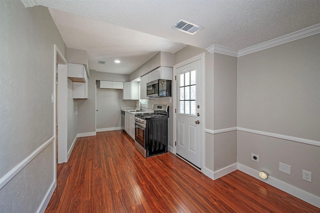 kitchen with a textured ceiling, stainless steel appliances, dark wood-type flooring, crown molding, and white cabinetry