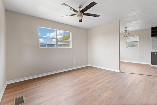 spare room with ceiling fan with notable chandelier, a textured ceiling, and light hardwood / wood-style flooring