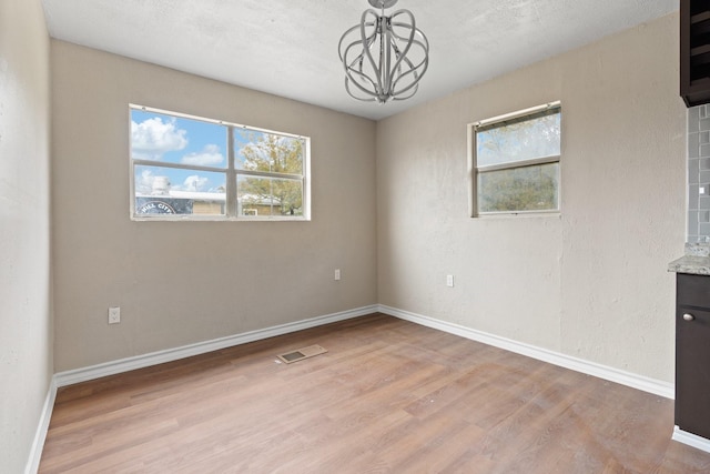 spare room featuring a chandelier, light hardwood / wood-style floors, and a wealth of natural light