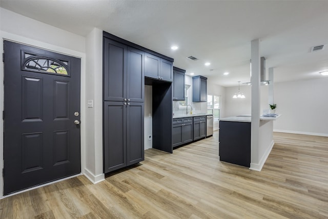 kitchen with a chandelier, stainless steel dishwasher, kitchen peninsula, pendant lighting, and light hardwood / wood-style floors