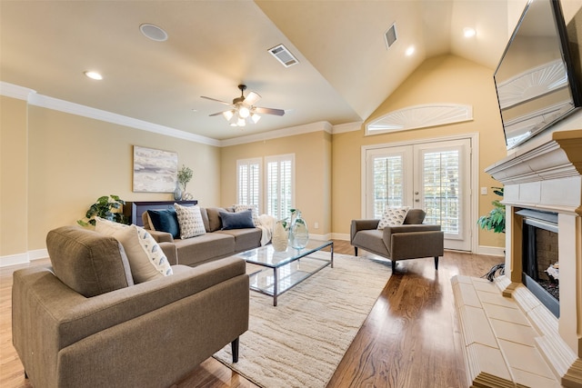 living room with ceiling fan, crown molding, lofted ceiling, a tiled fireplace, and light wood-type flooring