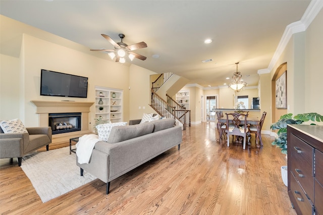 living room featuring ceiling fan with notable chandelier, light hardwood / wood-style floors, and crown molding