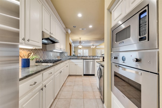 kitchen featuring appliances with stainless steel finishes, tasteful backsplash, stacked washer / dryer, white cabinets, and light tile patterned flooring