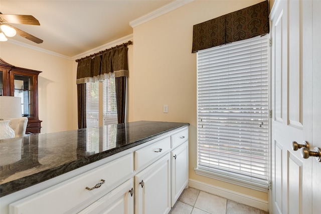 kitchen featuring light tile patterned floors, dark stone counters, white cabinetry, and crown molding