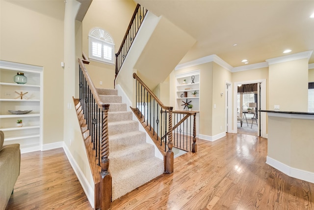 stairs with hardwood / wood-style floors, built in features, and crown molding