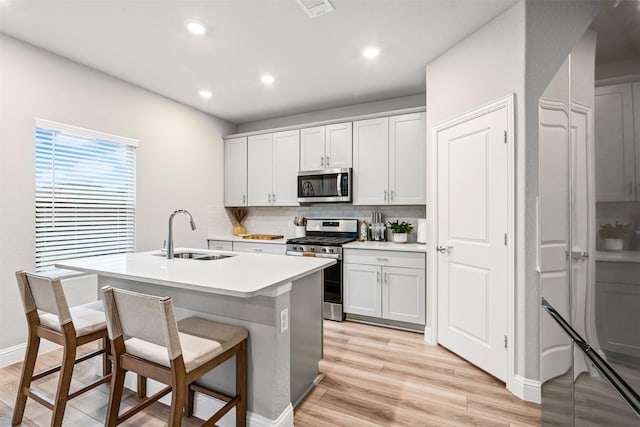 kitchen featuring backsplash, sink, light hardwood / wood-style flooring, an island with sink, and stainless steel appliances