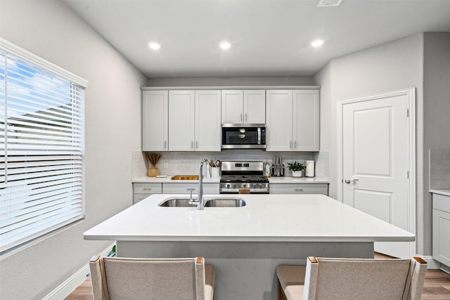 kitchen with a center island with sink, sink, light hardwood / wood-style flooring, decorative backsplash, and appliances with stainless steel finishes