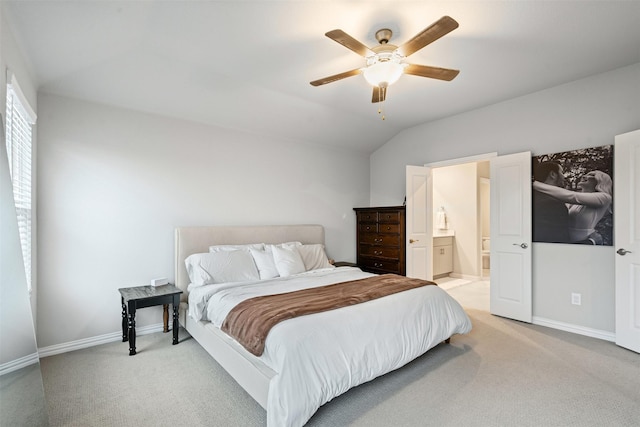 bedroom with ceiling fan, ensuite bath, light carpet, and vaulted ceiling