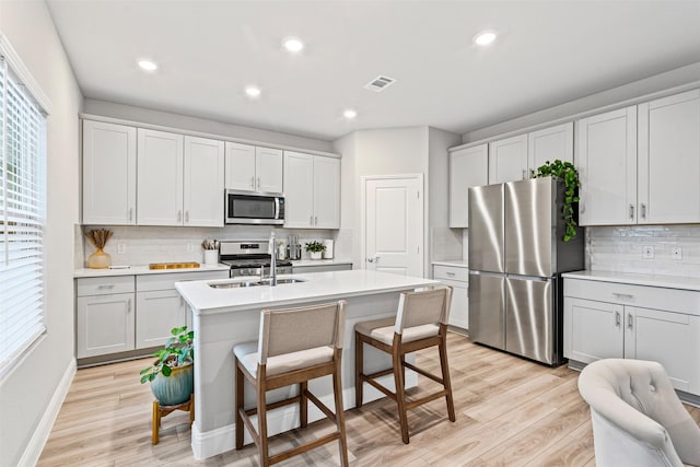 kitchen featuring stainless steel appliances, light hardwood / wood-style flooring, plenty of natural light, and a center island with sink